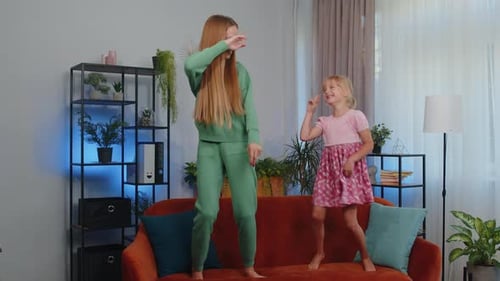 Happy Two Teenage Girls Siblings Best Friends Couple Dancing at Home Room on Couch Disco Party