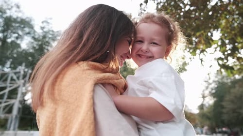 Loving mother walks with her cute daughter in the park. Mom holds her daughter in her arms, they lau
