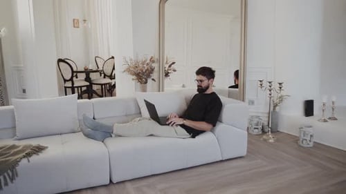 Man Works on Laptop While Lying on Sofa