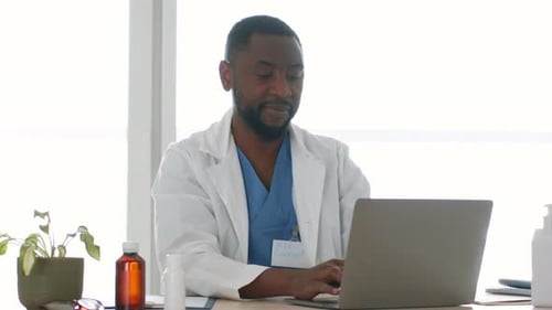 Young Professional African American Man Doctor in Robe Working on Laptop at Office Smiling to Camera