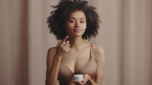 Woman Applying Moisturizer to Face and Smiling