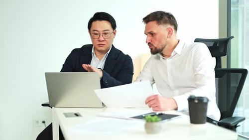 Businessmen Collaborating on Paperwork and Laptop in Office Meeting