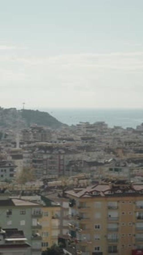Vertical video. View from a high point on the roofs of houses in a coastal town with the sea in the