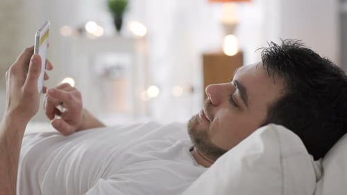 Man Using Mobile Phone Lying on Bed Indoors