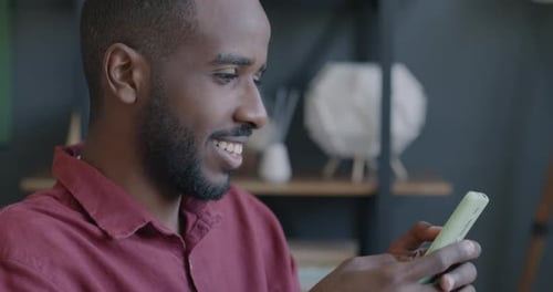 Cheerful African American Man Entrepreneur Using Smartphone Messaging and Smiling in Office
