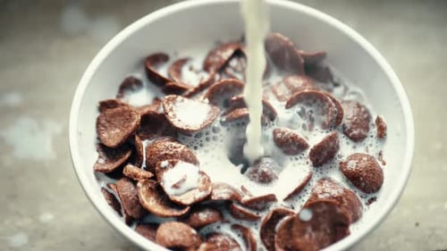 Milk Pours onto Chocolate Cereal in White Bowl