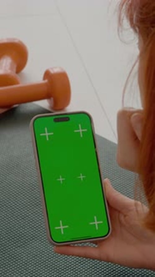 Vertical video Woman checks smartphone while resting on gym mat during workout session