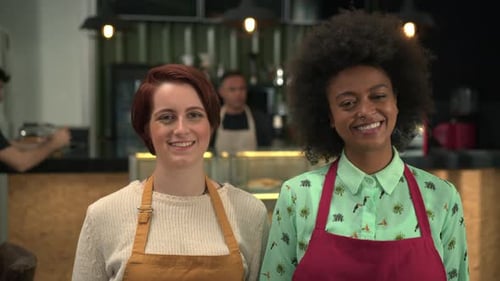 Two happy waitresses working at a cafe. Diverse young women wearing aprons smiling