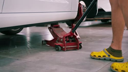 White luxury car being lifted with a red wheel change jack at a car service during detailing and dry