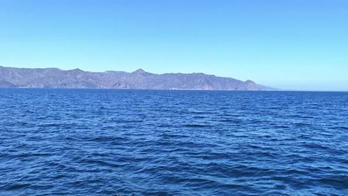 Island in the distance view from the ocean with boat of to the side blue water and sky