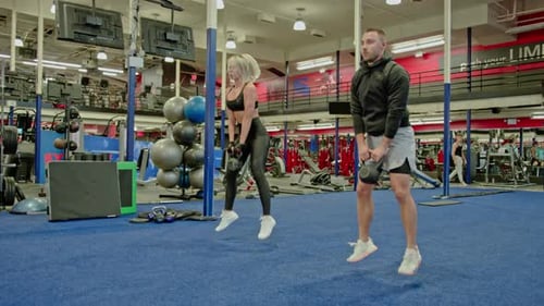 Man and Woman Exercising with Kettlebells in Gym