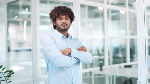 Portrait of a young serious handsome man in a shirt standing in modern office. Confident male indian