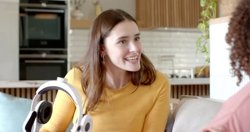 Holding VR headset, woman sitting on couch talking to friend at home