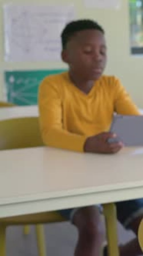 Vertical video: Reacting to peer approaching boy yellow shirt in class adjusting tablet, glancing