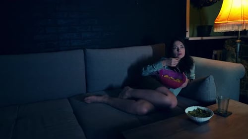 Slow Motion Footage of Pretty Caucasian Lady Lying in Comfortable Living Room and Eating Chips