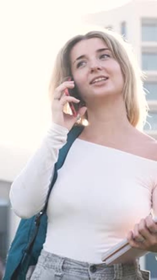 Young Woman Engaging in a Joyful Phone Conversation While Surrounded By Campus Life