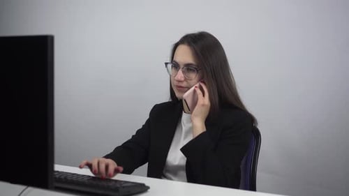 A Young Businesswoman Works at a Pc and Speaks on the Phone