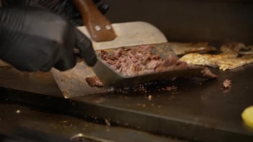 Cook uses spatula and scraper to toss flip and cut beef fajitas cooking on flat top griddle, slow