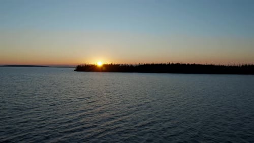 Drone flying along the water of a lake and slowly moving up to reveal a pretty sunset