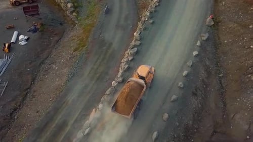 Fully loaded dump truck leaves construction. site dirt road and continues onto a paved road.