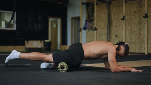 Man Massages Thigh on Foam Roller in Gym