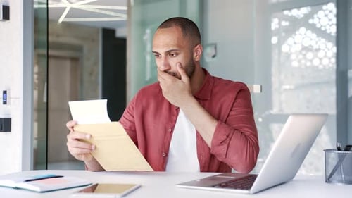 Upset disappointed businessman reading a letter with bad news sitting in a business office. Worried