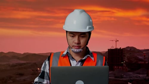 Asiatischer männlicher Ingenieur arbeitet auf einer Baustelle an einem Laptop, Bergbaumaschinen