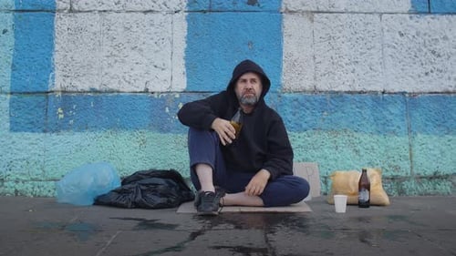 Homeless Poor Drunk Man Sitting on the Ground in the City and Yell to People Agression After He