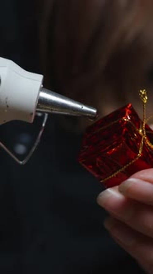 Vertical video. A young woman puts hot glue on a Christmas tree decoration, for a festive decoration