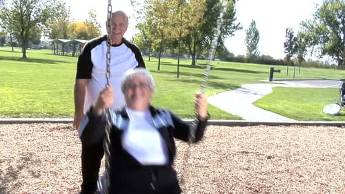 Senior man pushing his wife on a swing in the summer park