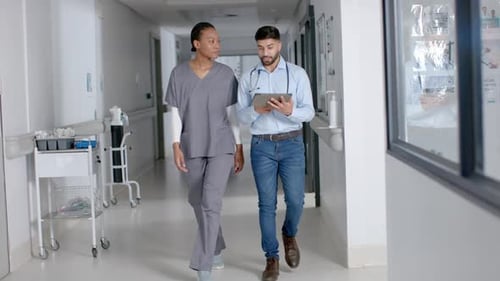 Diverse male and female doctors discussing work using tablet in hospital corridor, slow motion