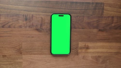 Smartphone with Green Screen on Wooden Desk, Office Workspace for Mockup or VFX Use