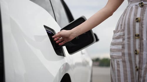Woman plugs in charger into socket of her modern new electric car