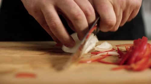 Chef Slicing Onion and Red Pepper on Cutting Board