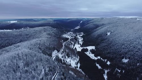 Aerial winter mountain road landscape covered in snow showing long horizon slow fly