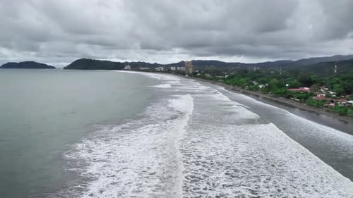 Waves crashing at the shore on the beach by the city.