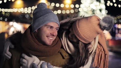 Romantic couple hugging at Christmas market at night