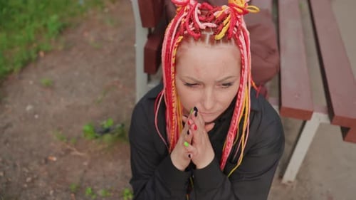 Thoughtful woman with colorful braids sits on bench