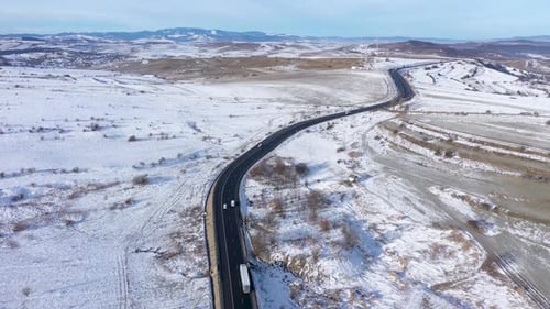 Luftaufnahme einer kurvenreichen Straße mit fahrenden Autos an einem frostigen Wintersonnentag in Zeitlupe per Drohne