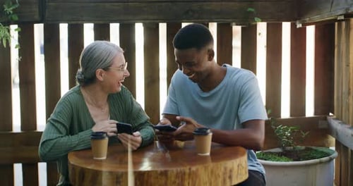Woman and Man Laughing, Looking at Phones at Cafe