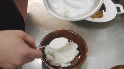 Chef prepares mediterranean starter yogurt dish. Adding yogurt from metal bowl into the plate. Close