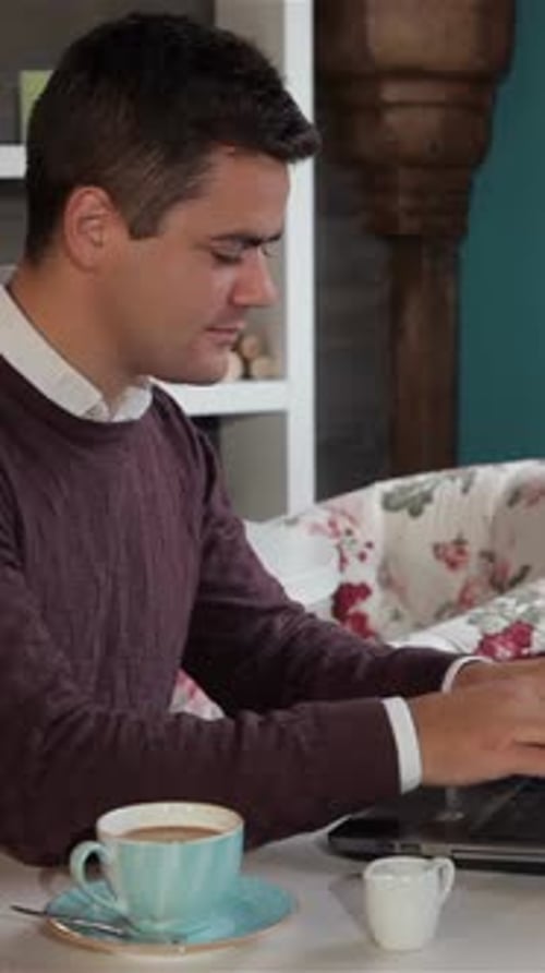 Focused Man Working on Laptop in a Cozy Cafe