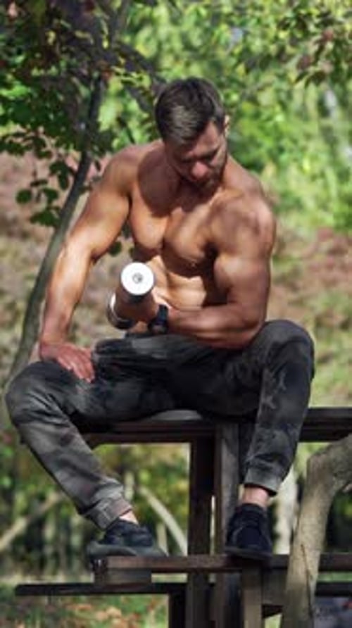 Muscular Man Lifting Dumbbell in Park