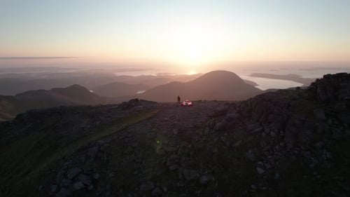 Hiker standing on the top of An Teallach mountain next to a unfolded tent during sunset in Scotland