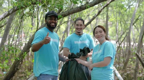 Tres voluntarios con un mono de trabajo recolectan basura y la depositan en una bolsa de plástico en el bosque.