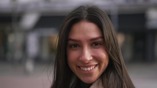 Portrait of a happy young brunette woman smiling at camera standing in urban city street. Confident