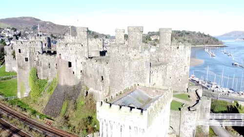 Medieval Conwy castle Welsh market town ruins aerial lowering view across historical towers and rail