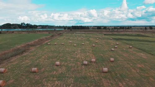 Drone Flies Over Field With Haystacks Against Backdrop Clouds River