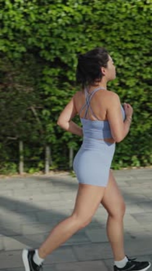 Woman Jogging Down Urban Path on Sunny Day