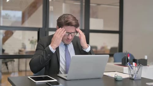 Middle Aged Businessman having Headache while Working on Laptop in Office